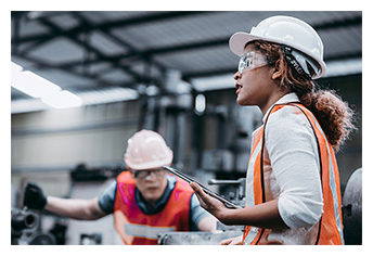 Factory workers wearing personal protective gear; one is holding an electronic tablet